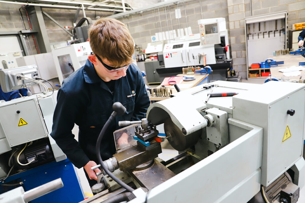A male student working on a machine in the correct uniform and equipment. Higher Technical Qualifications - Herefordshire Ludlow and North Shropshire College Group
