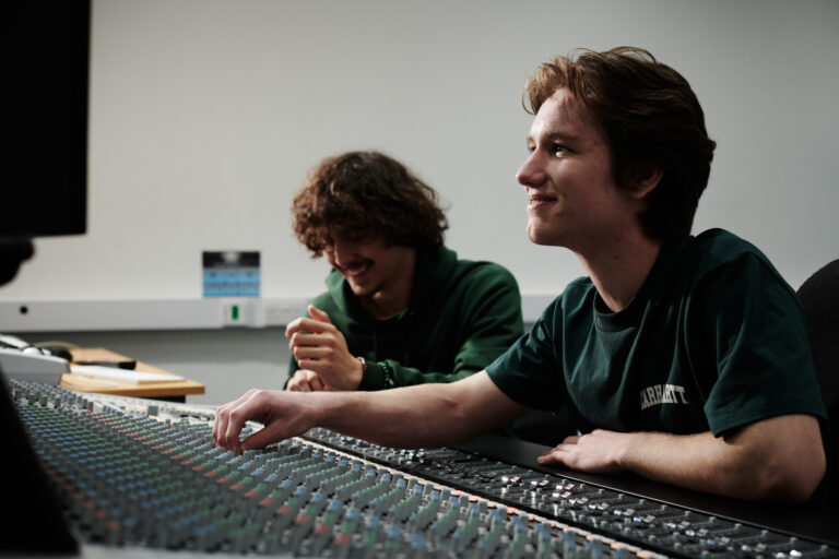 Two male students smiling, using an audio mixer deck at Herefordshire College