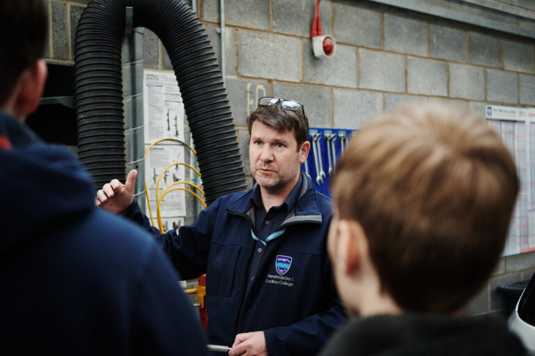 A male teacher talking to a group of male students in a garage at Herefordshire College
