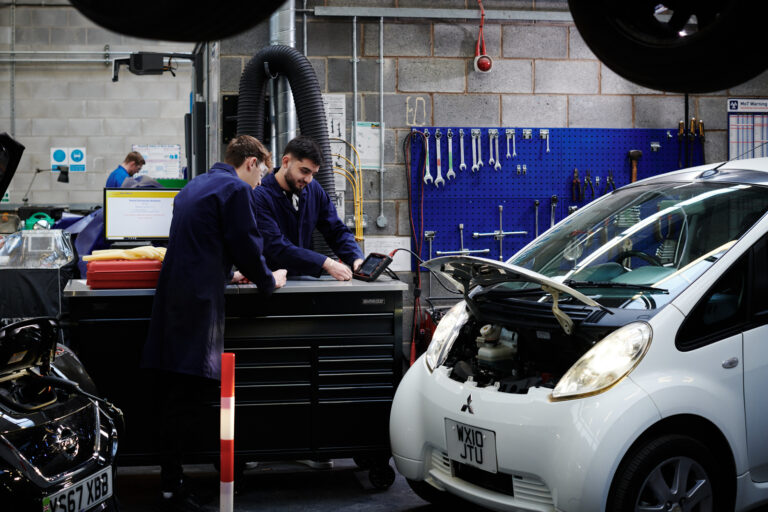 Two male students concentrating and using equipment in a garage setting at Herefordshire College