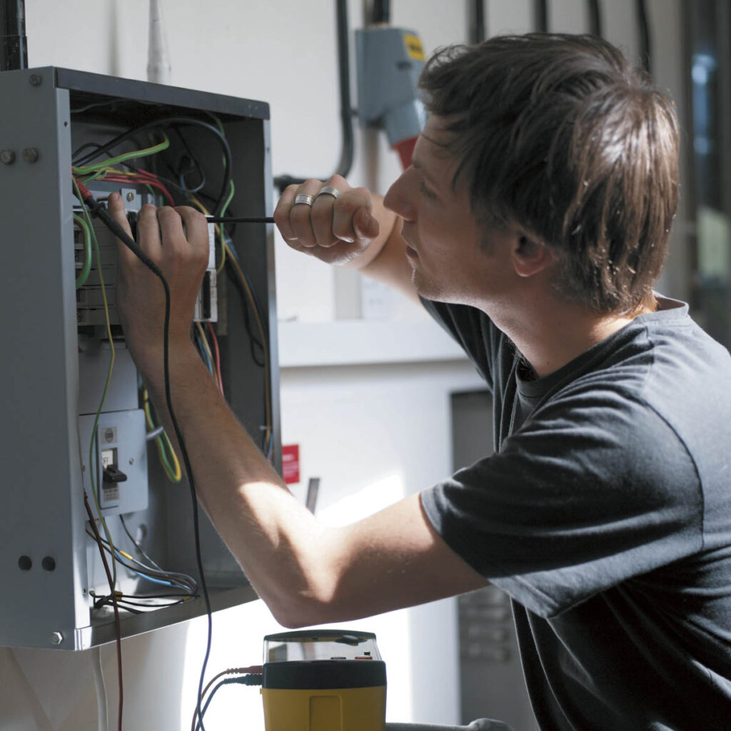 A student using a screw driver when working on an electricity fuse box.