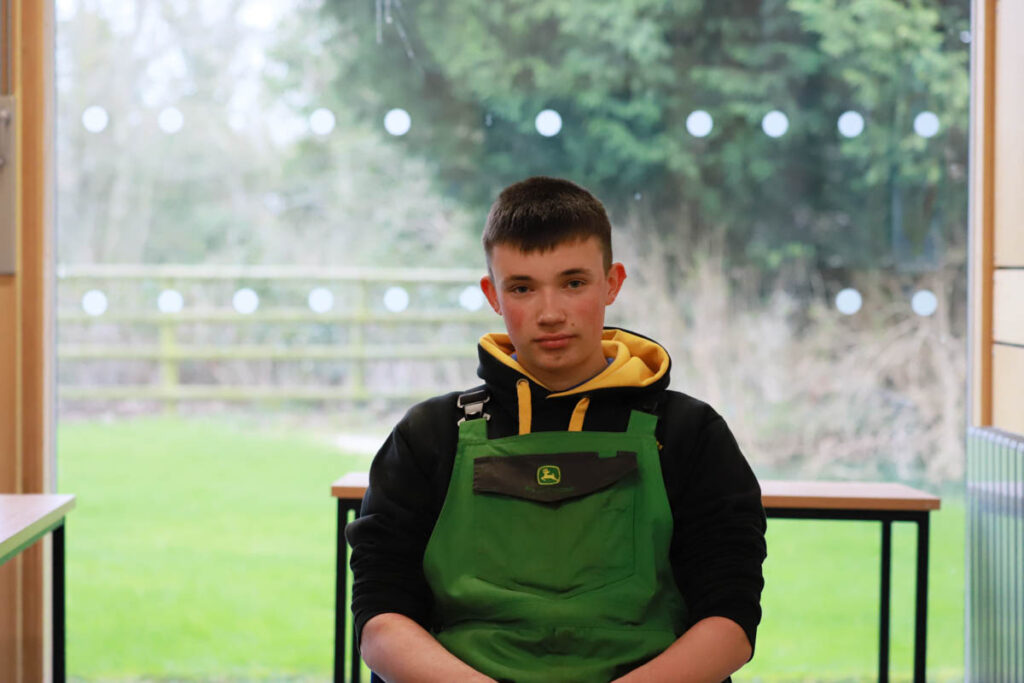 A student in a classroom wearing John Deer protective clothing, at Holme Lacy College