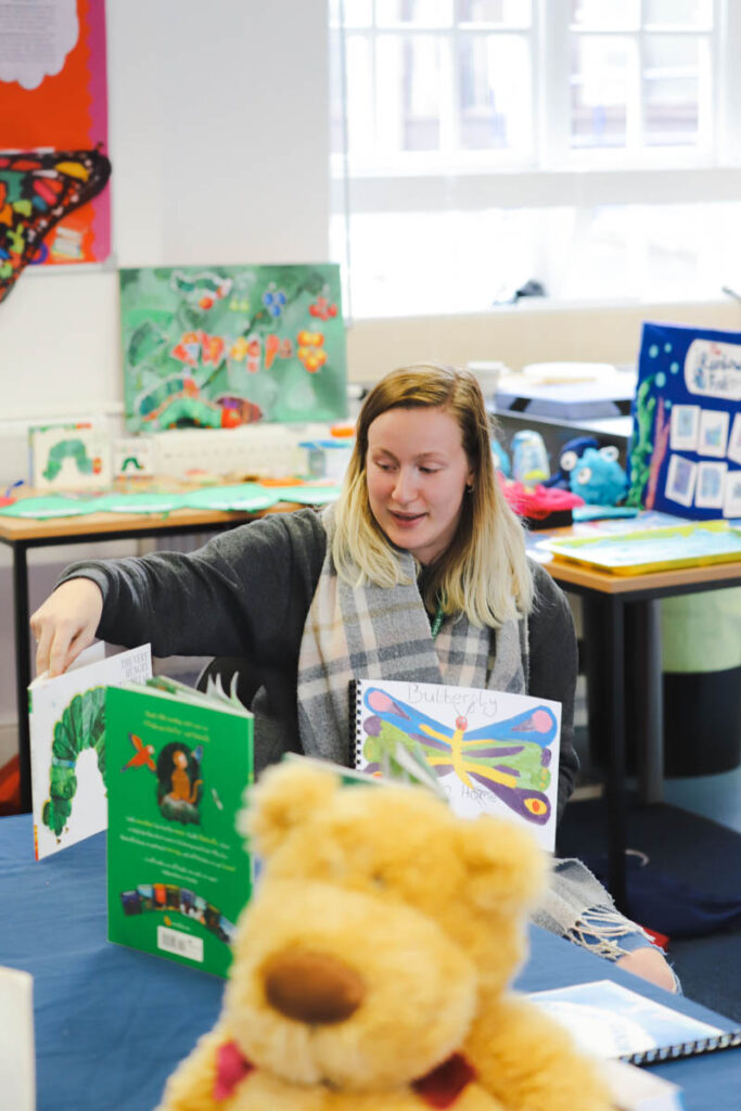 A female holds up student art work and children's books in a primary teaching classroom at the HLNSC Ludlow College.