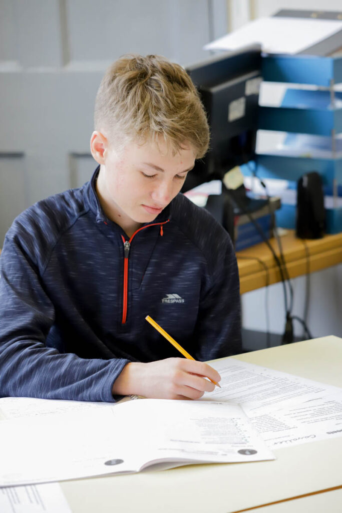 A male student writes on worksheet in a classroom at the HLNSC Ludlow College.
