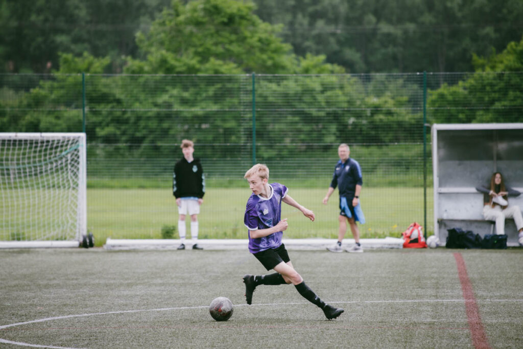 A shot of a male student playing football on an astro turf pitch at Ludlow College, in a purple kit being supported by the side line