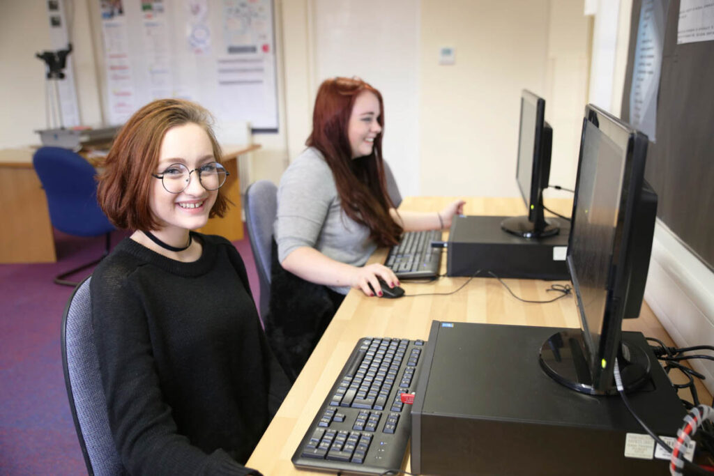 Two female students smiling and using computers at Ludlow College