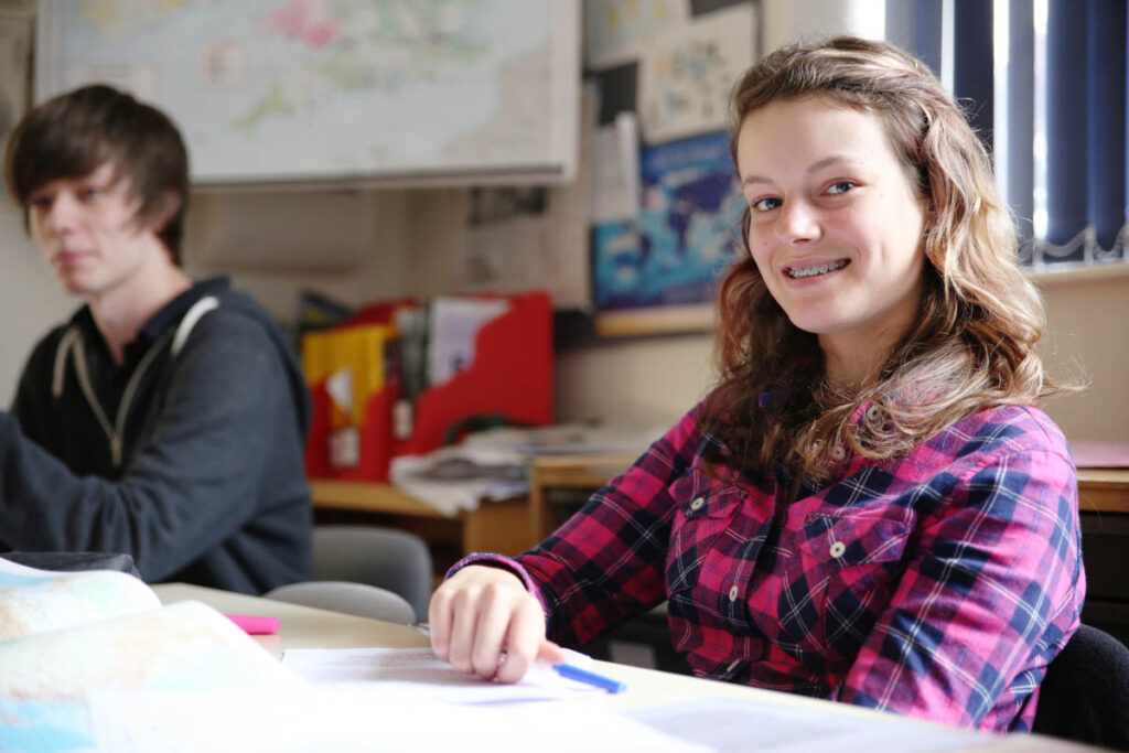 A female student smiling in a classroom seated next to a male student at Ludlow College