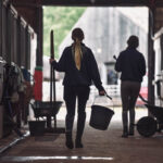 The back of two female students in a stable holding cleaning equipment at Walford College