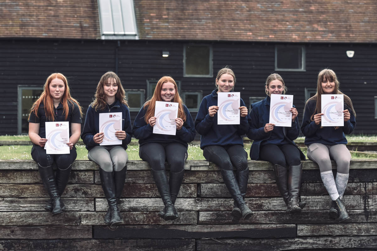 Six female students smiling and sat on a wall holding certificates at Walford College