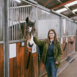 A female student posing next to a horse in an stable