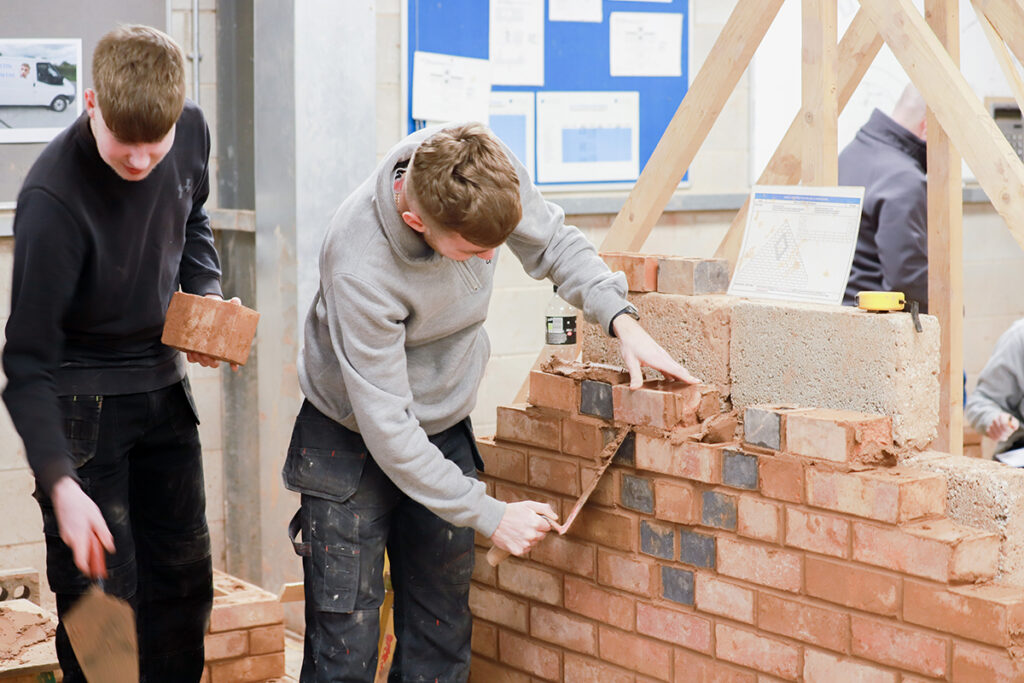 Two male students participating in bricklaying in a workshop environment