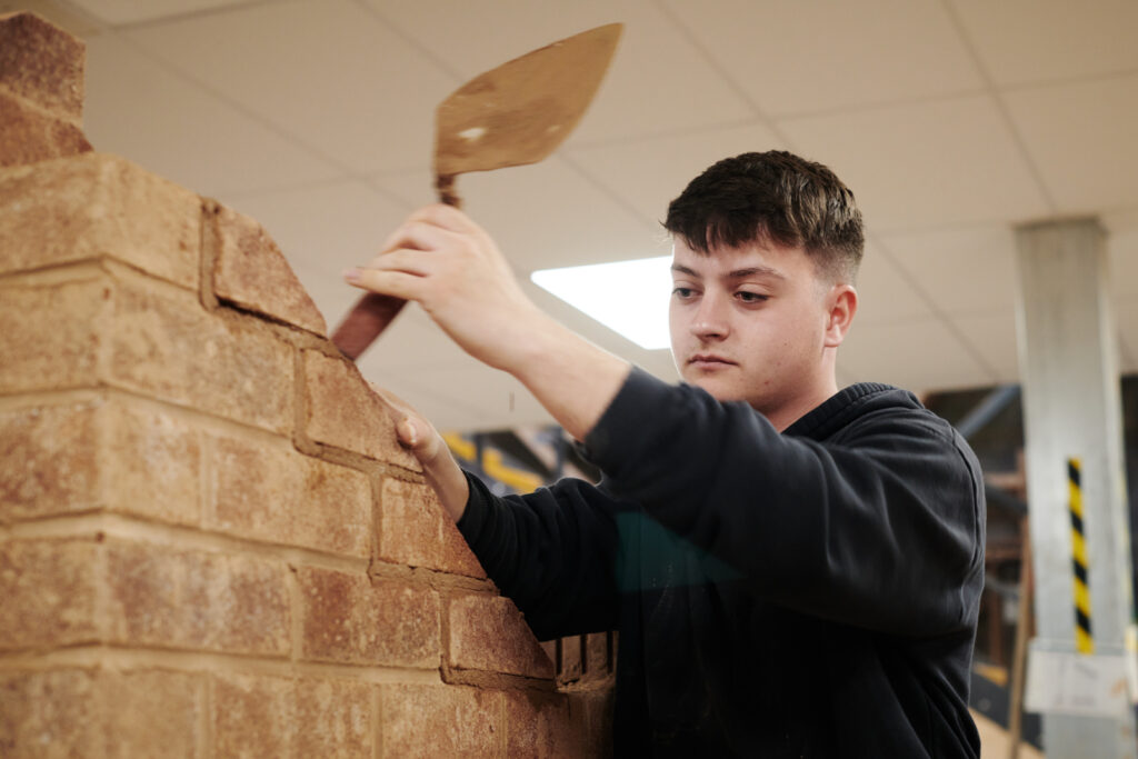 student laying bricks down with cement