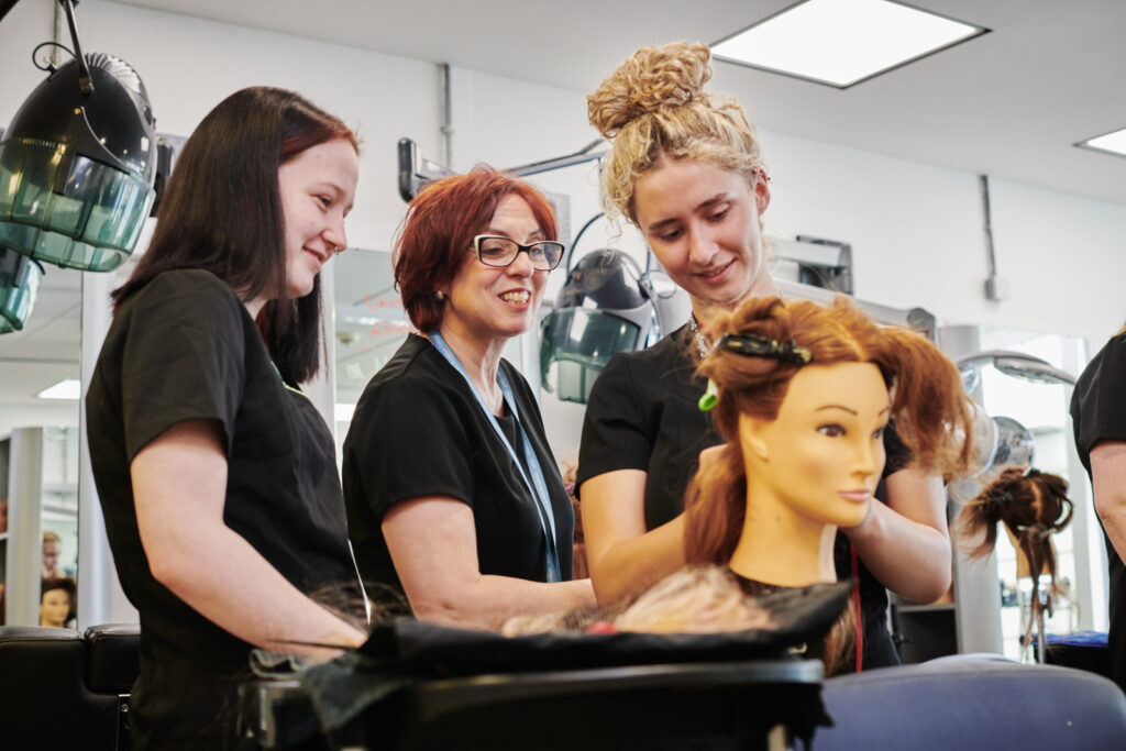 two students working on a models hair at Herefords hair and beauty studio with the lecturer watching to check if they are doing it properly