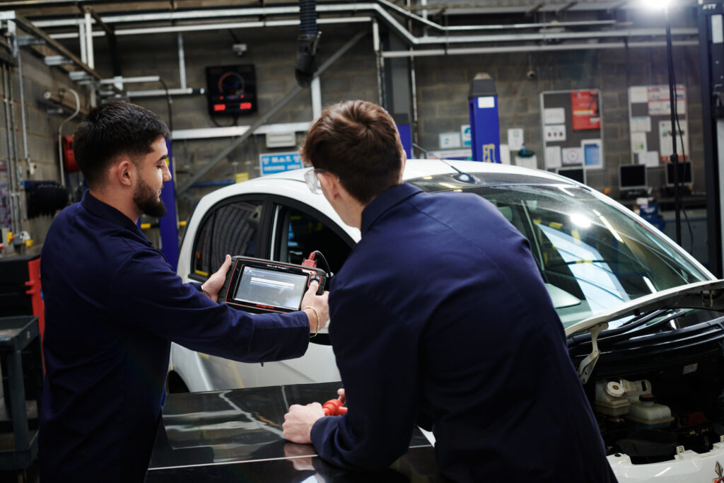 a picture of two students working on a electric car charging in the motor vehicle workshop