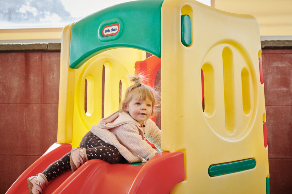a young girl playing on a plastic slide in the play area in the colleges nursery
