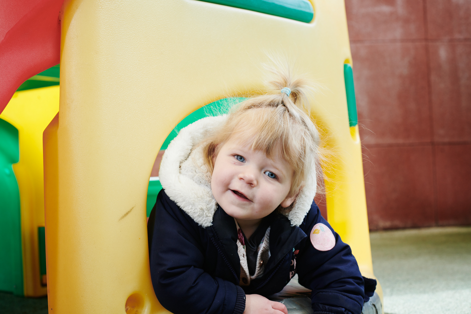 a young girl playing on a plastic slide in the play area in the colleges nursery
