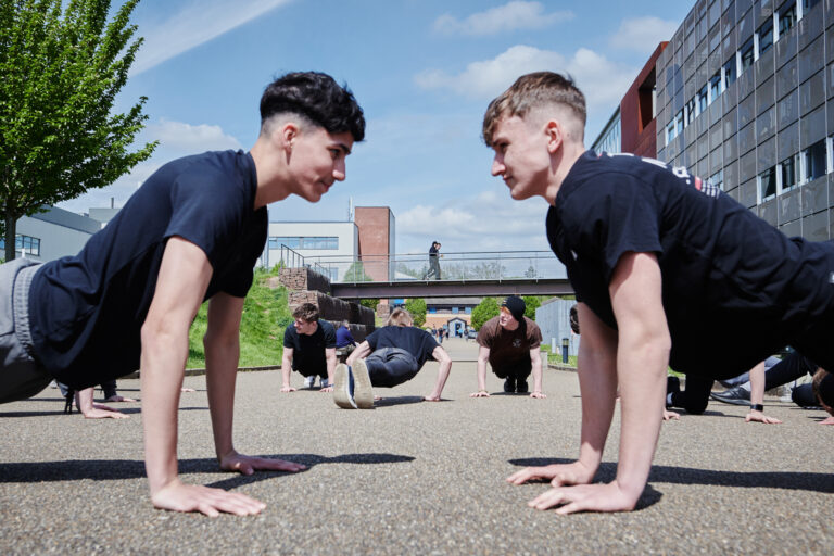 a group of public services students doing press-ups outside of the building on the tarmac