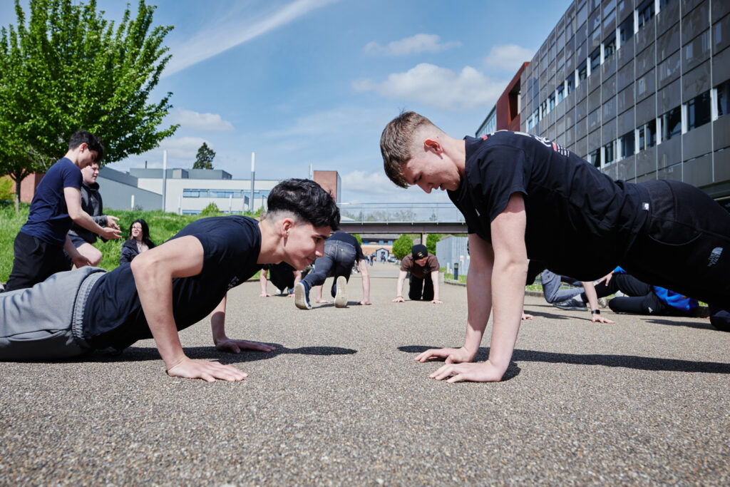 a group of public services students doing press-ups outside of the building on the tarmac
