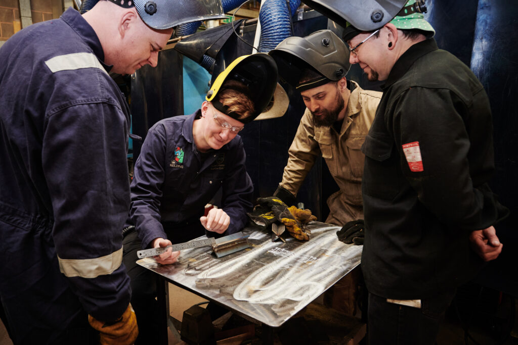 Group of welders in protective gear measuring metal