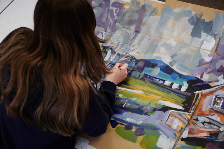 Female student painting on a piece of cardboard in Art class at Ludlow College