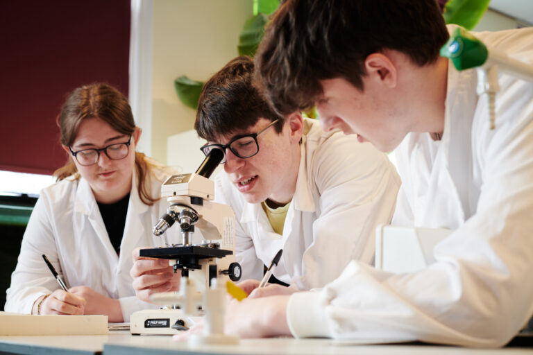Three students in correct protective wear using equipment and technology for a task in Biology at Ludlow College