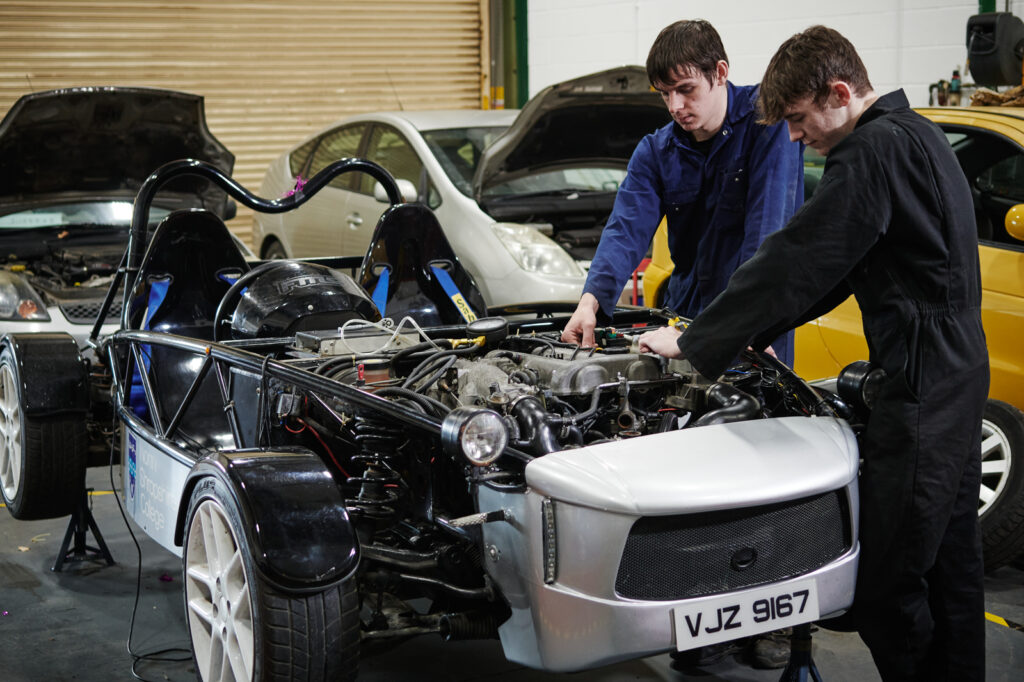 A shot of two male students in correct uniform working on a car engine in a garage environment at Walford College