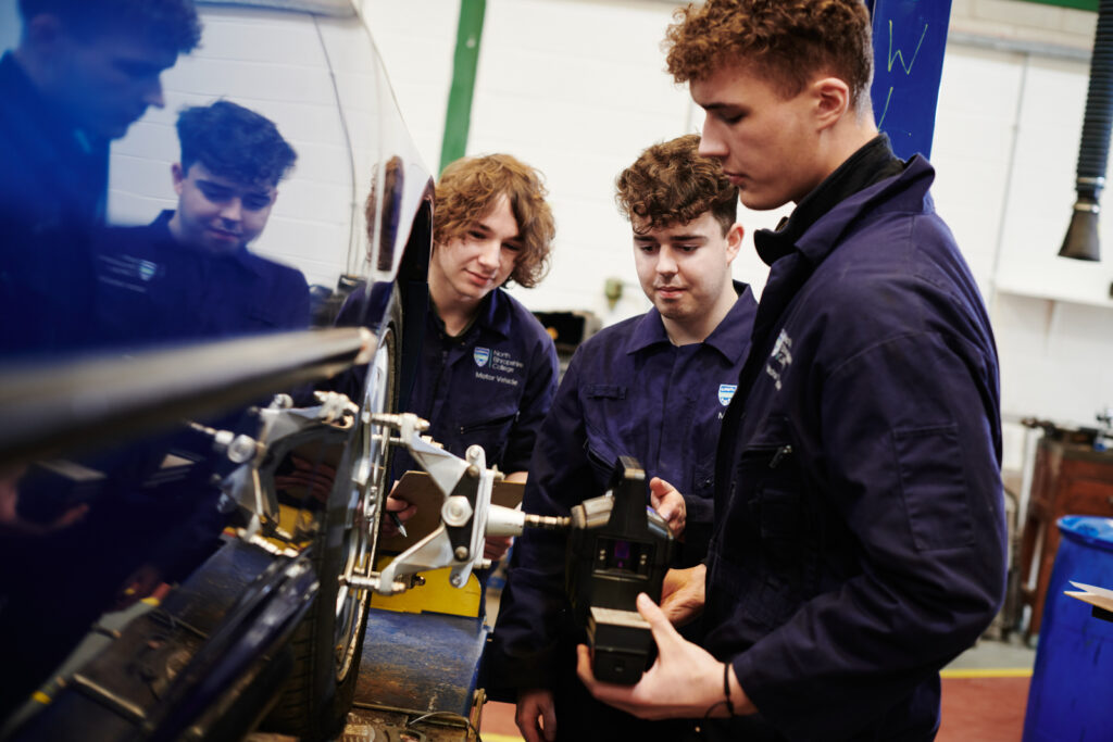 Three male students in the correct uniform working on a car wheel with equipment in a garage environment at Walford College