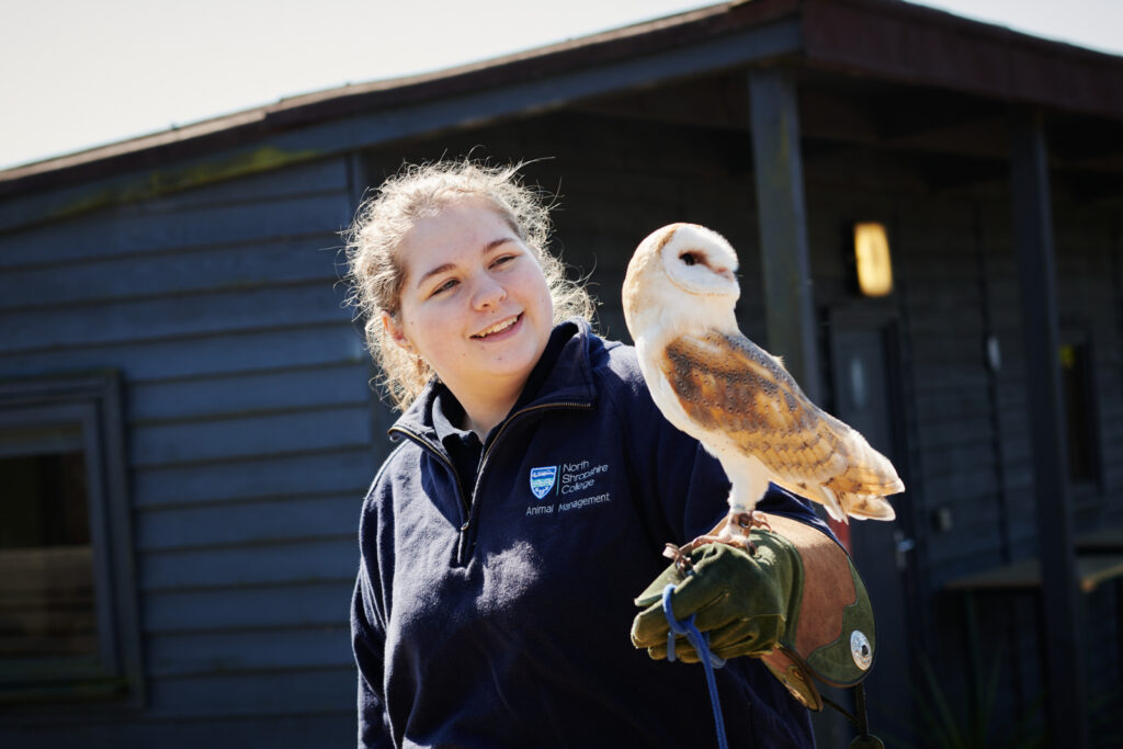 A female student in correct uniform and protective gear smiling and holding an owl outside at Walford College