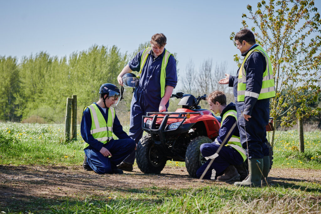 A long shot of three male students and a supervisor looking at a single quad bike in correct uniform outside at Walford College