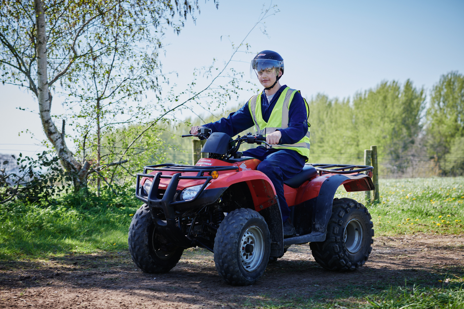 A male student in correct uniform and protection on a quad bike in the outdoors at Walford College