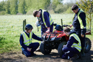 Three male students and a supervisor looking at a single quad bike in correct uniform outside at Walford College