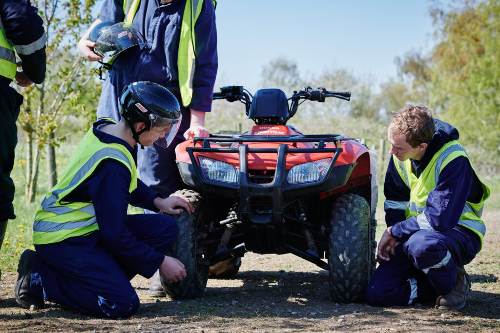 Two male students kneeling and looking at a quad bike in correct uniform outside at Walford College