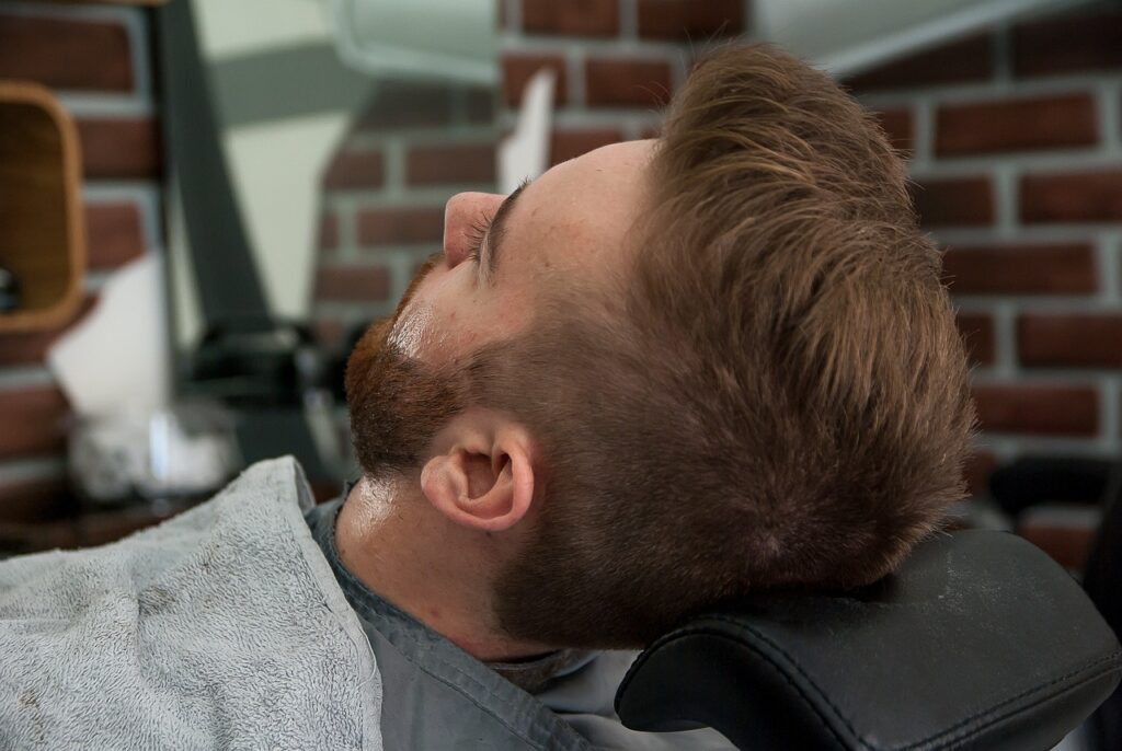 barber trimming beard in hairdressing salon chair