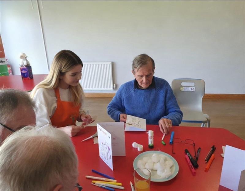 “Health and social care student Ellie sitting with an elderly man during a work placement